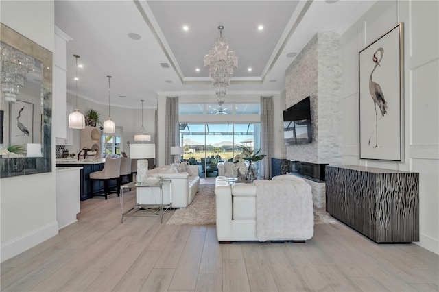 living room with a raised ceiling, light hardwood / wood-style flooring, a chandelier, and ornamental molding