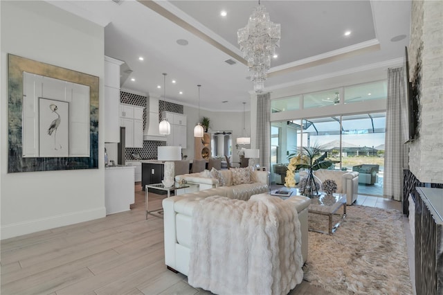 living room featuring light hardwood / wood-style floors, a raised ceiling, a fireplace, a chandelier, and ornamental molding