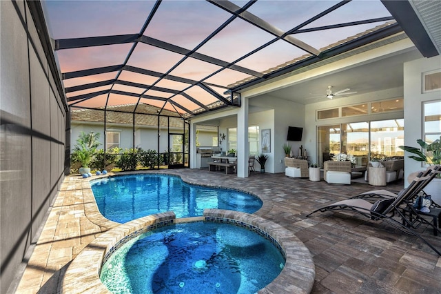 pool at dusk with ceiling fan, a patio area, glass enclosure, and an in ground hot tub