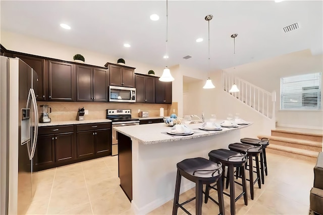 kitchen featuring hanging light fixtures, stainless steel appliances, backsplash, dark brown cabinets, and light tile patterned flooring