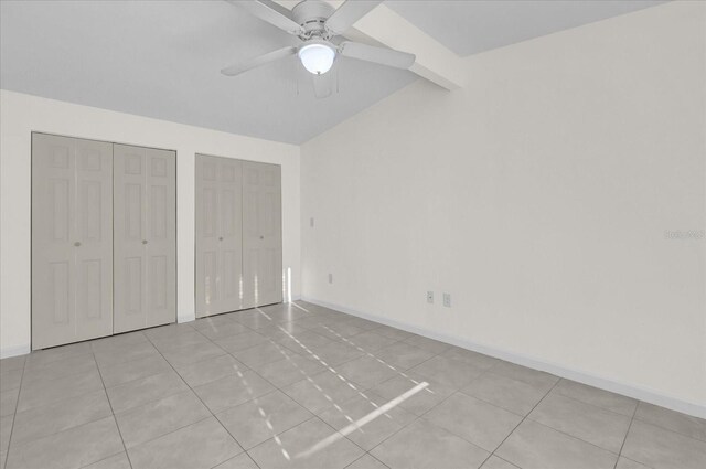 unfurnished bedroom featuring vaulted ceiling with beams, ceiling fan, light tile patterned floors, and two closets