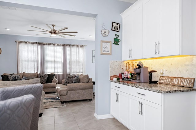 interior space with white cabinetry, ceiling fan, backsplash, dark stone counters, and light tile patterned floors