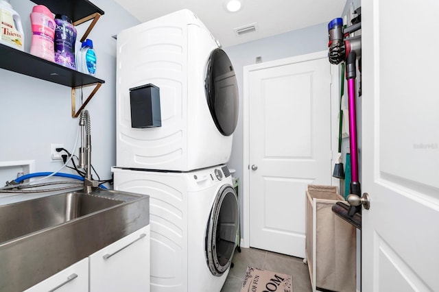 clothes washing area featuring light tile patterned floors and stacked washer and clothes dryer