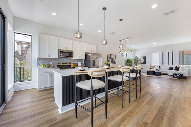 kitchen with stainless steel appliances, tasteful backsplash, pendant lighting, a kitchen island with sink, and white cabinets