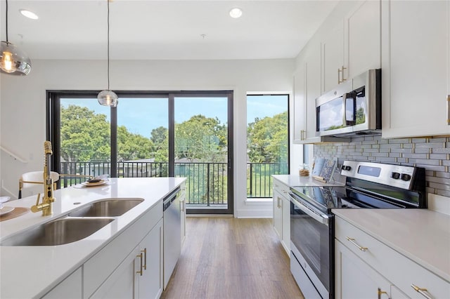 kitchen featuring white cabinetry, sink, stainless steel appliances, decorative light fixtures, and light wood-type flooring