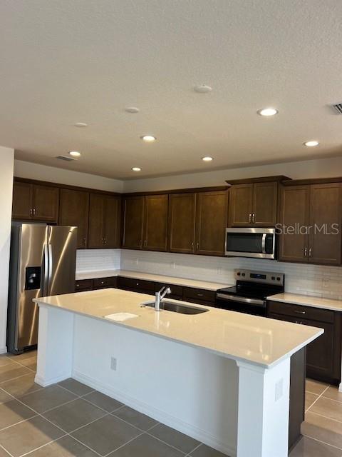 kitchen with sink, light tile patterned floors, stainless steel appliances, and an island with sink