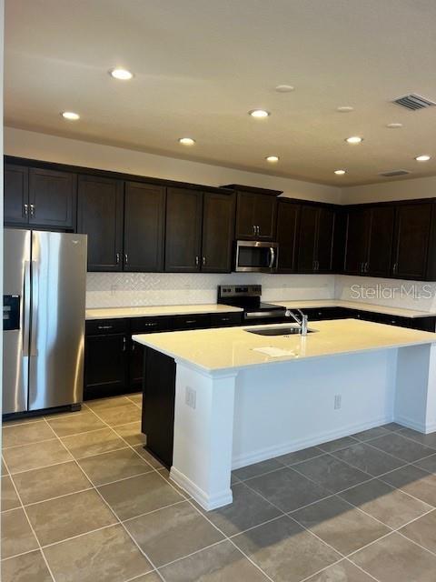 kitchen featuring light tile patterned flooring, appliances with stainless steel finishes, a center island with sink, and sink