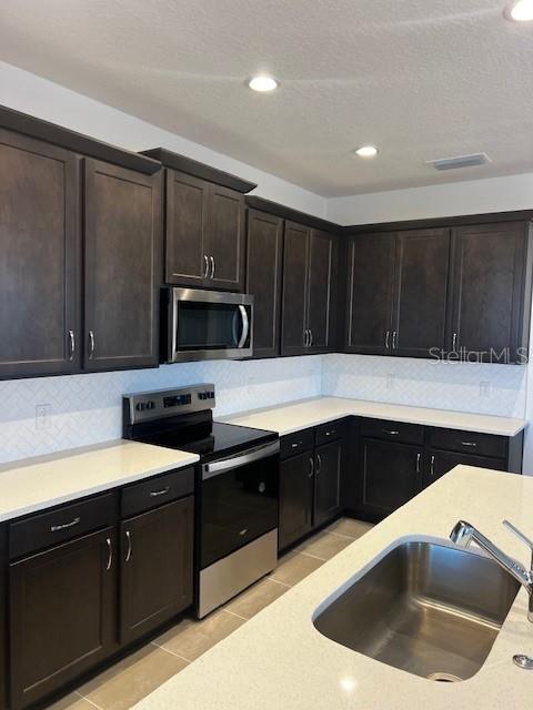 kitchen featuring dark brown cabinetry, sink, stainless steel appliances, backsplash, and light tile patterned flooring