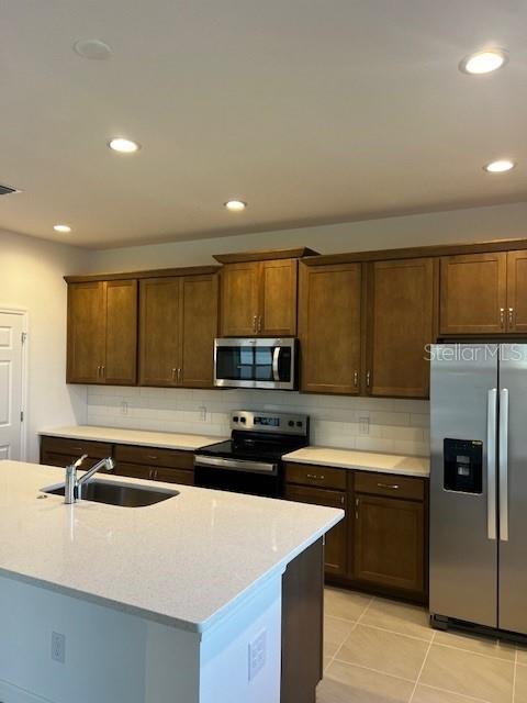 kitchen featuring light stone countertops, sink, stainless steel appliances, backsplash, and light tile patterned flooring