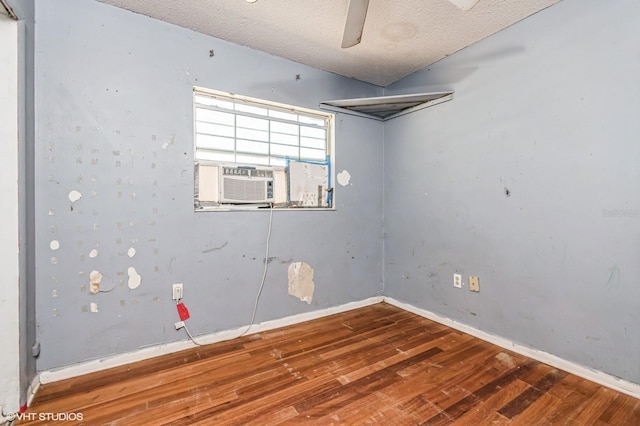 empty room featuring cooling unit, a textured ceiling, baseboards, and wood finished floors