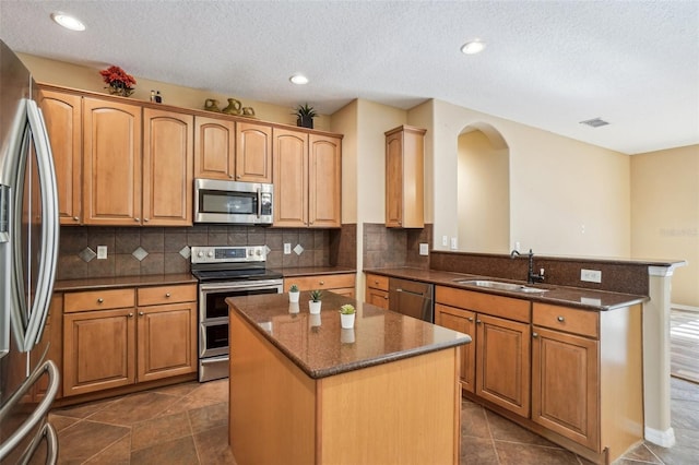 kitchen featuring kitchen peninsula, appliances with stainless steel finishes, a kitchen island, and sink