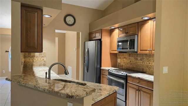 kitchen with light stone countertops, sink, kitchen peninsula, decorative backsplash, and appliances with stainless steel finishes