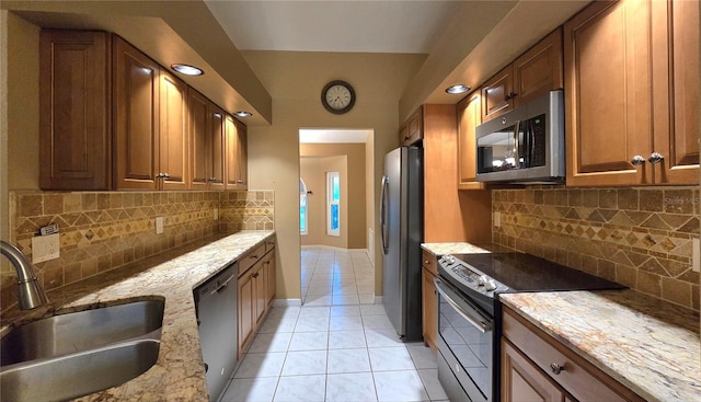 kitchen with light stone countertops, sink, backsplash, light tile patterned floors, and appliances with stainless steel finishes