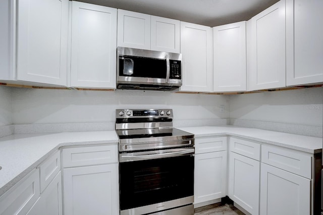 kitchen with white cabinets, appliances with stainless steel finishes, and light stone countertops