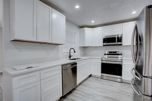 kitchen featuring sink, light hardwood / wood-style floors, a textured ceiling, white cabinets, and appliances with stainless steel finishes