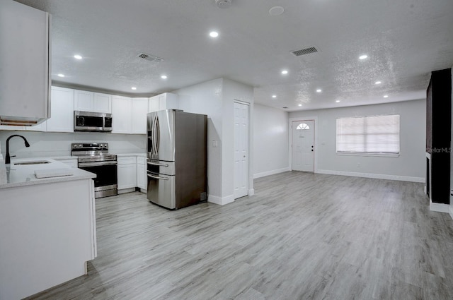 kitchen with appliances with stainless steel finishes, light wood-type flooring, a textured ceiling, sink, and white cabinetry