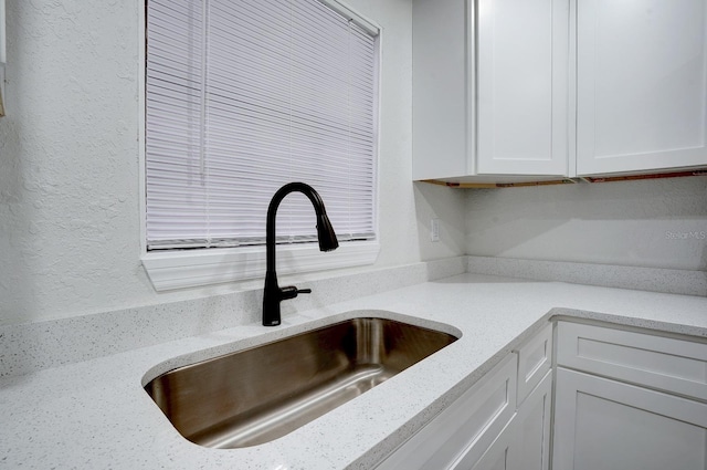 room details with light stone counters, white cabinetry, and sink