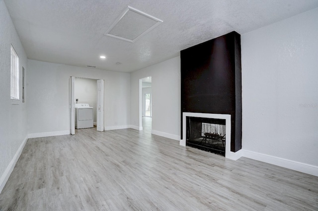 unfurnished living room featuring a multi sided fireplace, a textured ceiling, light wood-type flooring, and washer / clothes dryer