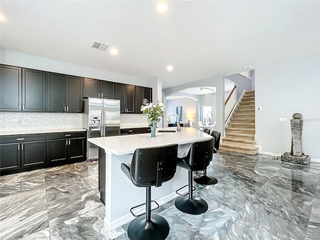 kitchen featuring dark brown cabinetry, stainless steel fridge with ice dispenser, backsplash, a breakfast bar area, and a kitchen island with sink