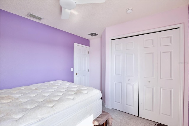 bedroom with ceiling fan, light colored carpet, a closet, and a textured ceiling