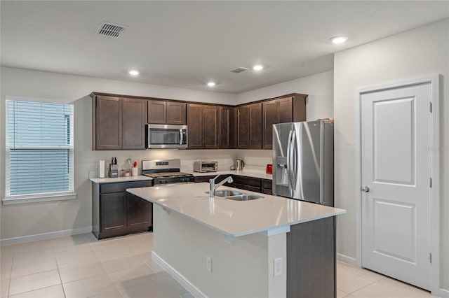 kitchen with dark brown cabinetry, sink, stainless steel appliances, a kitchen island with sink, and light tile patterned floors