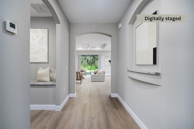 hall featuring arched walkways, wood finished floors, visible vents, and baseboards