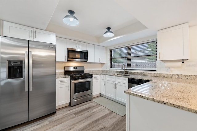 kitchen featuring a tray ceiling, white cabinets, appliances with stainless steel finishes, and sink