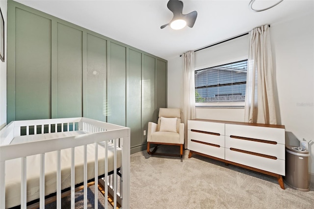 carpeted bedroom featuring ceiling fan and a nursery area