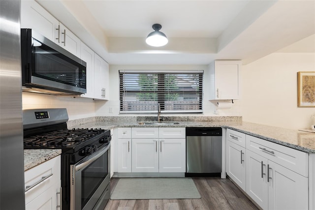 kitchen with stainless steel appliances, dark hardwood / wood-style flooring, white cabinets, light stone counters, and sink