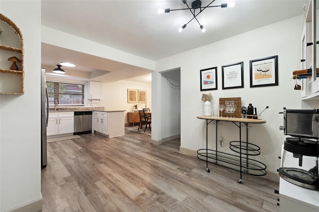 kitchen featuring white cabinets, stainless steel appliances, a chandelier, and light wood-type flooring