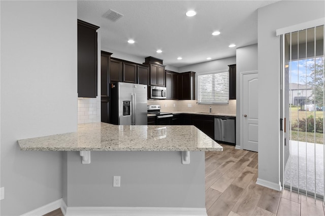 kitchen featuring backsplash, a kitchen breakfast bar, appliances with stainless steel finishes, light stone counters, and kitchen peninsula