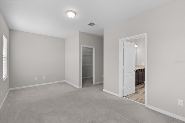 unfurnished bedroom with light carpet, a closet, a spacious closet, and ensuite bath