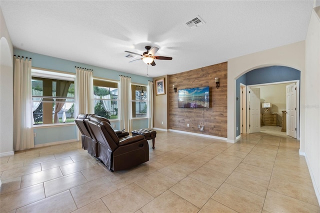 tiled living room featuring a textured ceiling, ceiling fan, and wooden walls