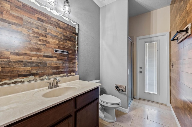 bathroom featuring tile patterned floors, wood walls, toilet, vanity, and a shower with shower door