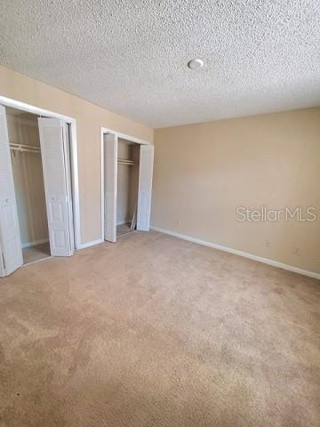 unfurnished bedroom with carpet flooring, a textured ceiling, and two closets