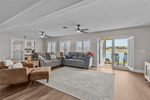 living room with a wealth of natural light, ceiling fan, light hardwood / wood-style flooring, and a water view