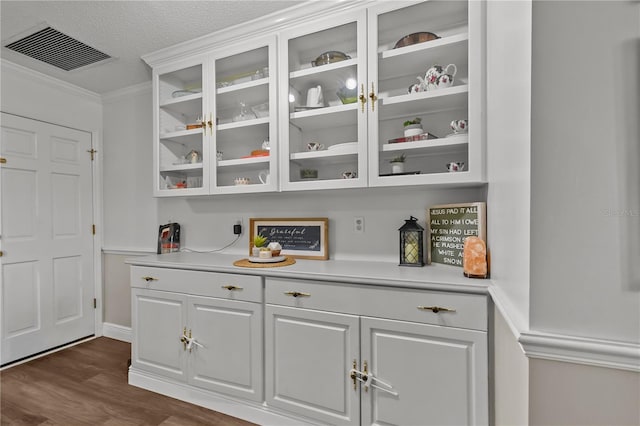 bar with a textured ceiling, dark hardwood / wood-style flooring, white cabinetry, and crown molding