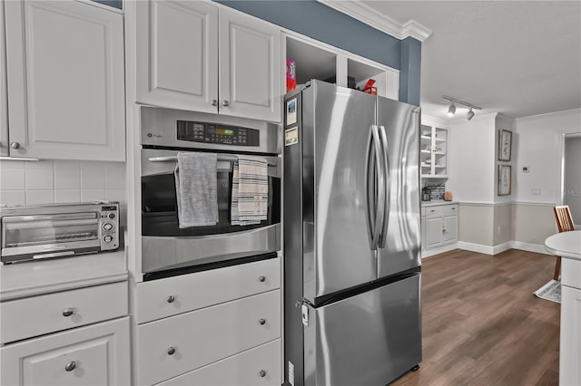 kitchen with appliances with stainless steel finishes, dark hardwood / wood-style flooring, track lighting, ornamental molding, and white cabinets