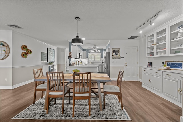 dining area featuring hardwood / wood-style floors, track lighting, ceiling fan, ornamental molding, and a textured ceiling