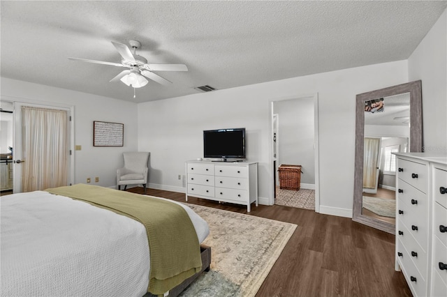 bedroom with ceiling fan, ensuite bathroom, dark wood-type flooring, and a textured ceiling