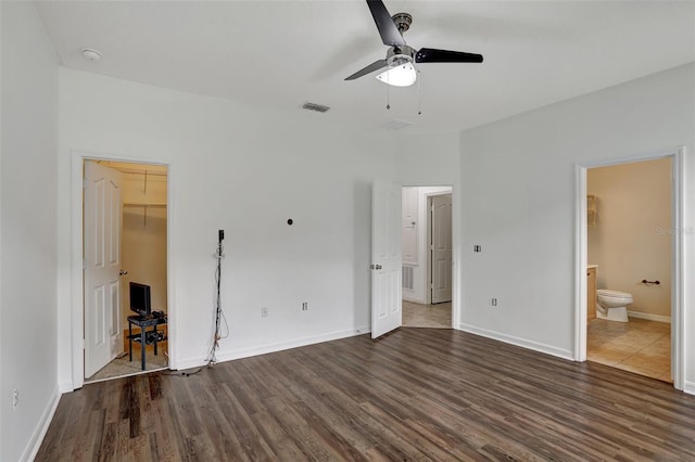 unfurnished bedroom featuring ceiling fan, dark hardwood / wood-style flooring, ensuite bathroom, a walk in closet, and a closet