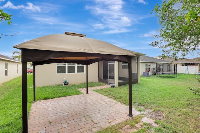 back of property featuring a yard, a trampoline, cooling unit, a gazebo, and a patio