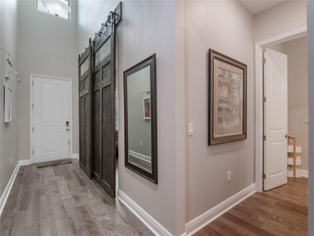 hallway featuring a barn door, a towering ceiling, and light wood-type flooring