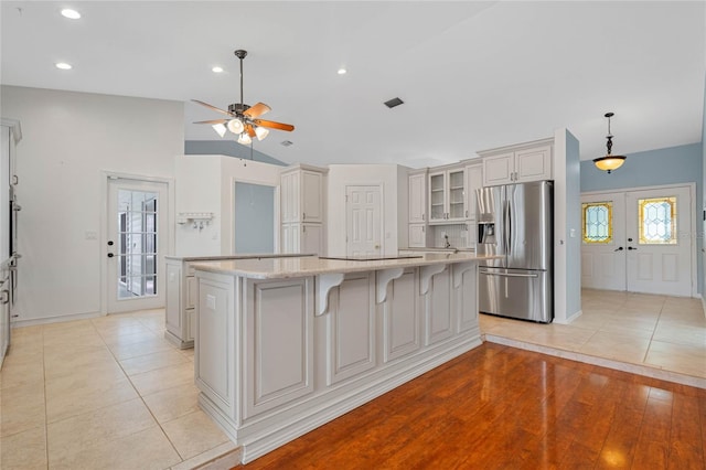 kitchen with a spacious island, stainless steel refrigerator with ice dispenser, hanging light fixtures, light tile patterned floors, and light stone countertops