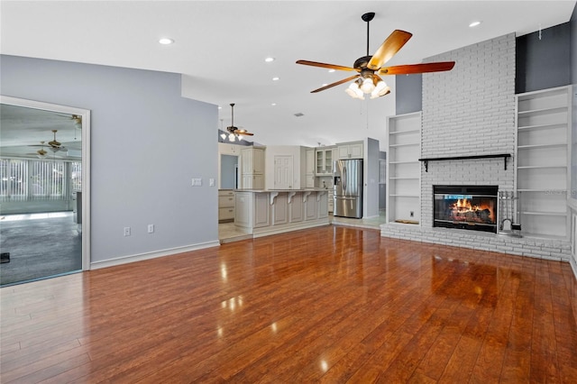 unfurnished living room featuring built in shelves, vaulted ceiling, light hardwood / wood-style flooring, and a brick fireplace