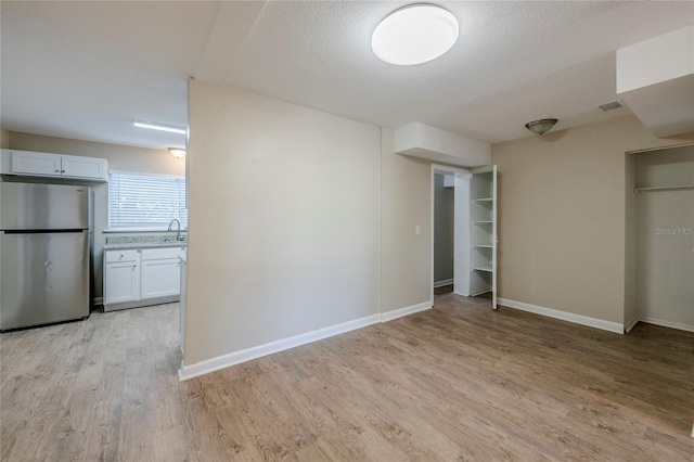 unfurnished bedroom featuring a textured ceiling, light hardwood / wood-style flooring, connected bathroom, and stainless steel refrigerator