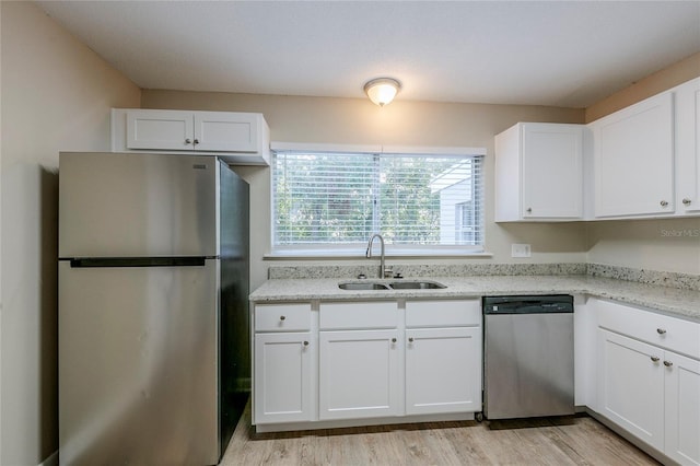 kitchen with light stone counters, stainless steel appliances, light wood-type flooring, white cabinetry, and sink