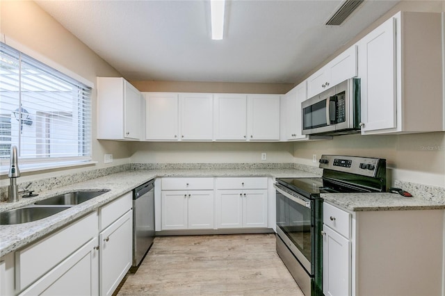 kitchen featuring light stone counters, light hardwood / wood-style floors, white cabinets, appliances with stainless steel finishes, and sink