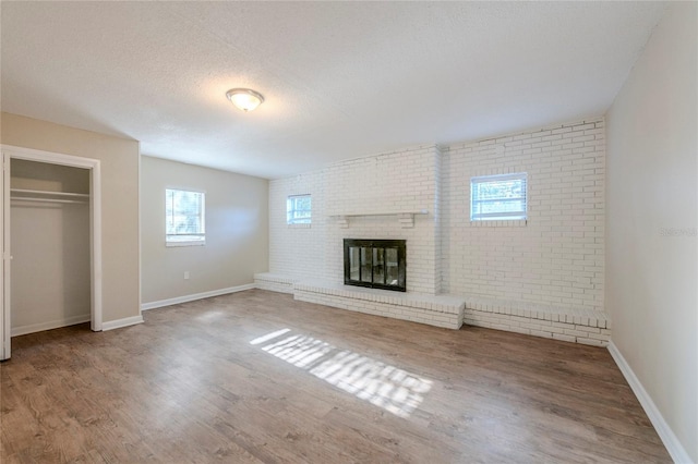 unfurnished living room featuring a fireplace, a textured ceiling, hardwood / wood-style flooring, and brick wall