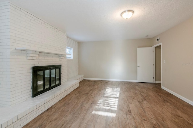 unfurnished living room featuring wood-type flooring, a brick fireplace, and a textured ceiling